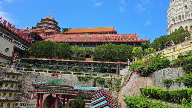 Kek Lok Si Buddhist temple complex on hillside in Penang, Malaysia. Colorful pagodas, shrines and white tower with golden spire surrounded by lush green trees. Traditional Asian architecture under blu