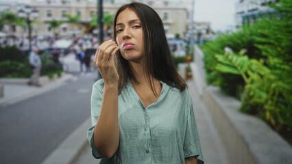 Fototapeta premium Young hispanic woman brunette with pinched fingers to face making a complaining gesture on a crowded street; annoyance demand.