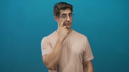 Man touching glasses with index finger and adjusting lens while wearing pink tshirt against teal backdrop in studio; thoughtful focus.