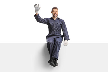 Male worker in a uniform and gloves sitting on a blank panel and waving