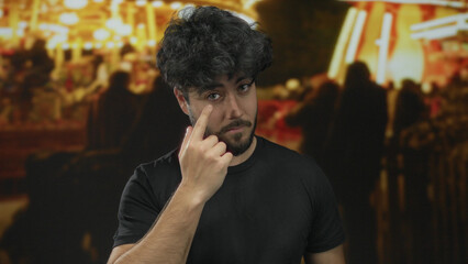 Young man with beard standing outdoors at night fair with blurred lights and people in background, capturing dynamic urban ambiance.