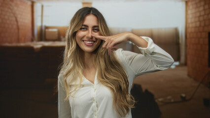 Young blonde woman finger pointing to nose on construction site; playfulness confidence cheerfulness optimism.