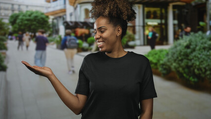 Young woman smiling while holding out her hand palm up on a busy city street, wearing a black t...