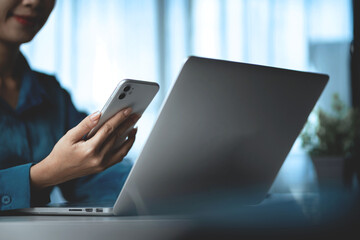 A woman is sitting at a desk with a laptop and a cell phone