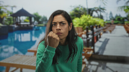 Fototapeta premium Woman with clenched fist and tense face at pool resort pier, leaning forward toward camera in a confrontational pose; anger confrontation.