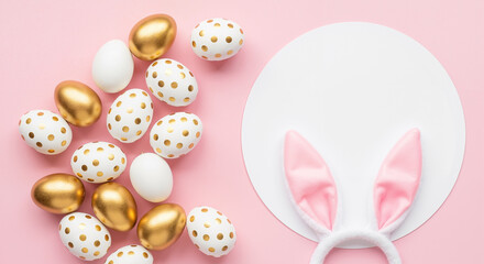 Easter flat lay with golden eggs, white polka dot eggs, and bunny ears on pink background with circular copy space.