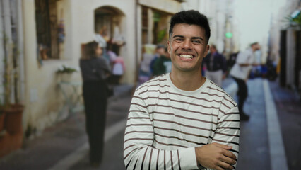 Fototapeta premium Handsome young man laughing on a city street wearing a striped shirt with people blurred in the background conveying a vibrant urban outdoor scene.
