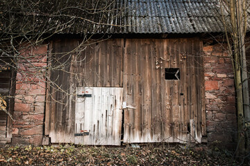 Old abandoned rural buildings. Decaying wooden door set in a cracked brick wall overgrown with plants. A symbol of passing time, neglect and forgotten places