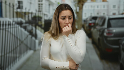 Woman outdoors displaying worry on a city street, surrounded by cars and buildings, expressing concern or anxiety during a moment of uncertainty in an urban environment.