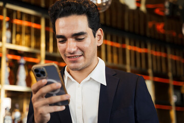 Confident young businessman checks his smartphone for important messages or data during a corporate event break in a luxurious hotel bar. Communication technology lifestyle. Browsing online
