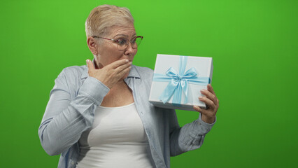 Woman holding gift box with hand to mouth gesture in studio with green screen; surprise joy...