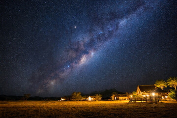 Milky Way over rustic cabins at night, starry sky long exposure astrophotography, warm village lights, dark-sky landscape, travel camping banner with copy space, high-res, nature backdrop.