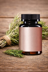 Supplement bottle mockup with blank rose-gold label on amber jar, black cap, rosemary on rustic wood. Minimal wellness packaging template, front view, copy space, high-res.