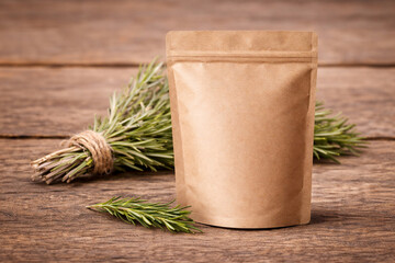 Blank kraft stand-up pouch packaging mockup on rustic wooden table with fresh rosemary bundle. Minimal eco branding template, front view, natural light, copy space, no logo, high-res.