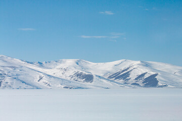 Fototapeta premium Wide angle sunset over frozen Lake Cildir, Kars, Turkey. Vast snow-covered ice sheet and dramatic sky in winter. Serene cold wilderness of Eastern Anatolia.