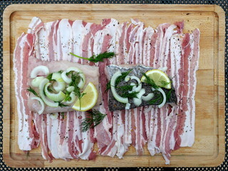 Preparation of hake fillets with bacon, onions, dill and lemon on wooden board. Fresh ingredients. Copyspace.