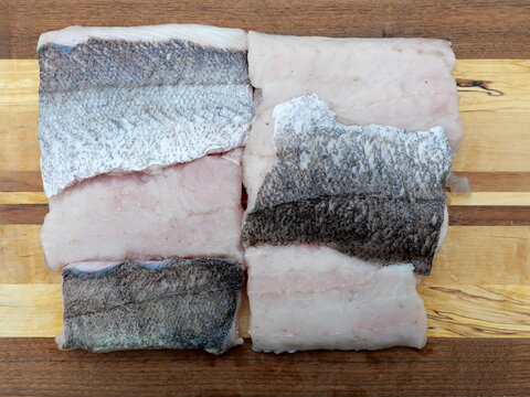 Raw European hake fillets arranged on a wooden cutting board. Fresh white fish meat, top view. Copyspace.