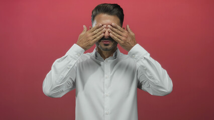 Young hispanic man with trimmed beard in white button shirt raises both hands open palms in studio;...
