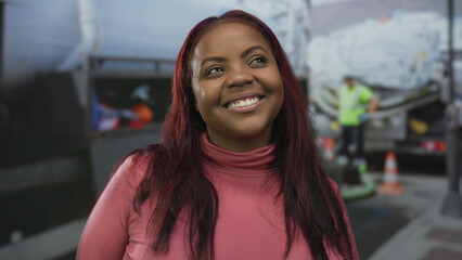 Woman in pink turtleneck sweater smiles while standing in brightly lit airport baggage conveyor...