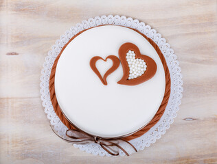 Overhead close-up of a celebratory white cake decorated with brown heart shapes and small, white...