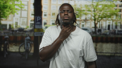 Man holding throat with hand on neck on street in amsterdam canal area appearing to choke or cough;...