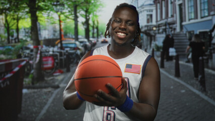 Man holds basketball with both hands, smiling in a white usa jersey and blue wristbands on a busy...