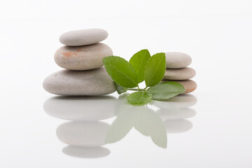 Stack of smooth zen stones with fresh green leaves, creatively arranged on a glossy white surface, promotes calmness and relaxation.