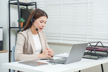 Asian businesswoman talking through headset during online meeting with client using laptop in office workspace providing customer support and digital consultation through communication technology