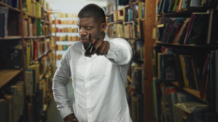 Man in white shirt standing with hands on hips and occasional pointing gesture among tall bookshelves in a library aisle inside building  frustration focus. © Krakenimages.com