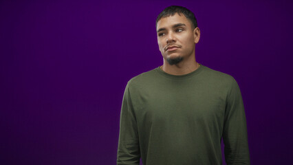 Obraz premium Man with visible face tilts head and shrugs slightly against a purple studio backdrop, wearing green shirt; quiet contemplation.