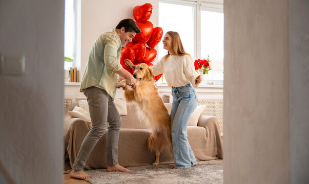 Joyful young couple playing and dancing with their dog at home, celebrating love, happiness and Valentine&rsquo;s Day together.
