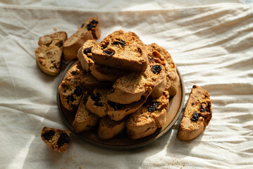 Stack of italian biscotti cantuccini cookies with nuts and raisins on a plate over white linen tablecloth