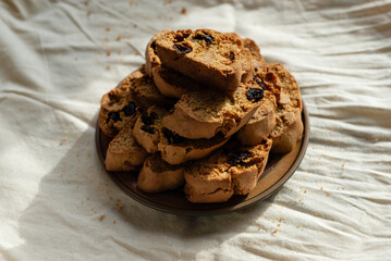 Italian biscotti cantuccini cookies with nuts and raisins on a plate over white linen tablecloth