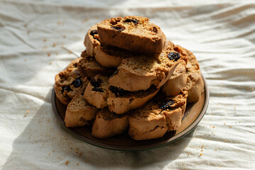 Stack of italian biscotti cantuccini cookies with nuts and raisins on a plate over white linen tablecloth