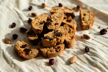 Italian cantuccini biscuits with hazelnuts and cranberries, served on a white linen tablecloth scattered with ingredients