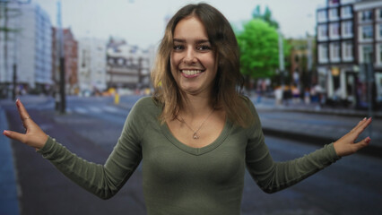 Fototapeta premium Young hispanic woman smiling with hands waving palms forward on a city street crossing wearing green shirt and heart necklace; joy.