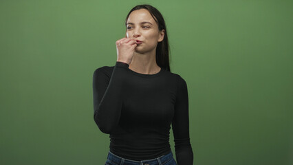 Woman with fingers pinched near lips performing a chef kiss gesture in a studio green backdrop; playful delight.