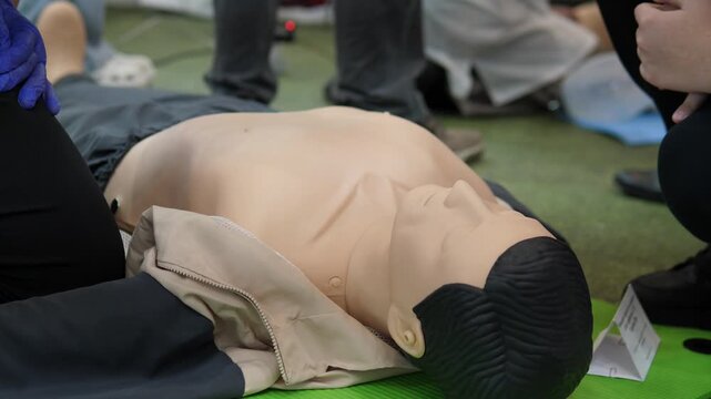 instructor guiding chest compression placement on mannequin with gloved hands focus on correct hand position and depth on green mat, quiet training room atmosphere, students kneel nearby