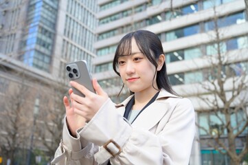 ビル街でスマホを使用する日本人ビジネスウーマン