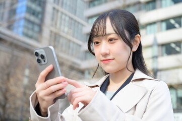 ビル街でスマホを使用する日本人ビジネスウーマン