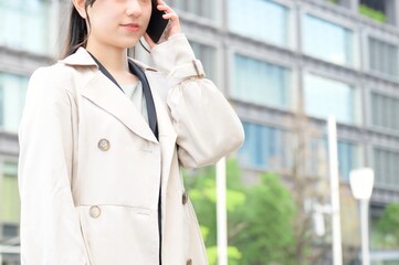 ビル街でスマホを使用する日本人ビジネスウーマン