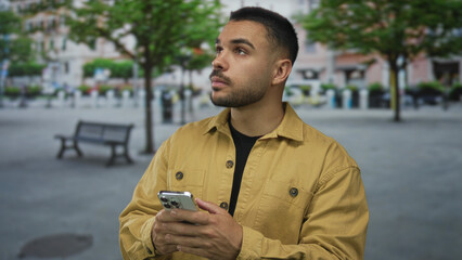 Man wearing brown jacket holding smartphone with bare hands on bustling urban street; digital...
