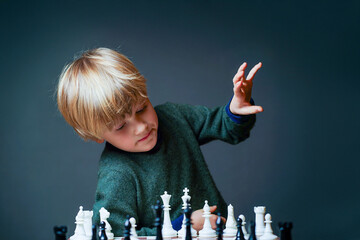 Young child playing chess, raising hand to make strategic move, symbolizing initiative, proactive decision making, courage to start, leadership thinking. Learning, education and critical thinking.