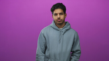 Obraz premium Man in gray hoodie shows thumbs down with visible thumb and neutral expression in studio; disapproval rejection.