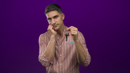 Man in striped shirt holding house key and hand on cheek while looking down in studio; contemplation decision.