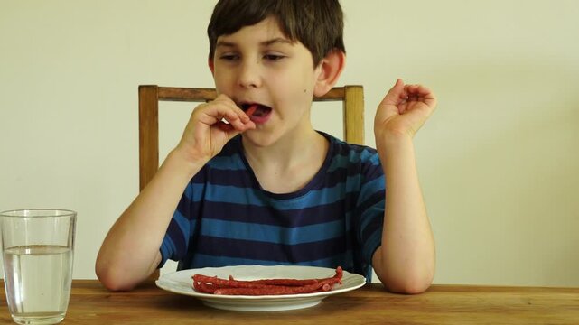 Boy eats dried cabanossi at the table

