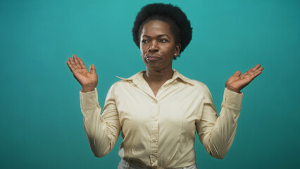 Woman raising both hands palms up in a shrug gesture wearing a cream shirt against a teal studio backdrop; resignation uncertainty.