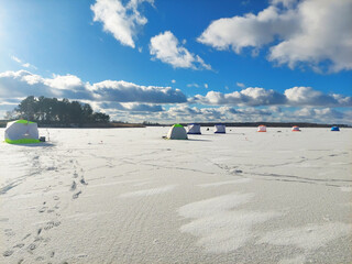 People set up tents on a frozen lake under a blue sky with clouds during winter in a remote area