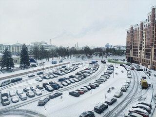 Vehicles parked in snow-covered area near buildings in winter season during daylight hours