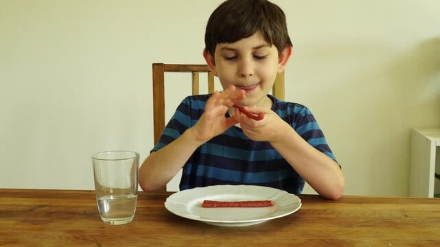 Boy eats dried cabanossi at the table

